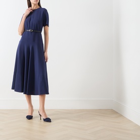 Model wearing Max Mara Studio navy dress with short sleeves, flared midi skirt and belt, styled with navy slingback heels.