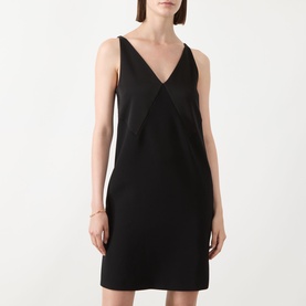 Model wearing black sleeveless V-neck mini dress with geometric panel detail, styled with a gold bangle bracelet.