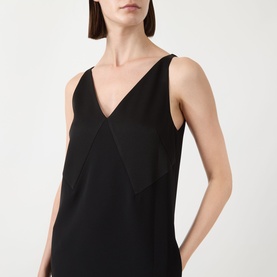 Model wearing black sleeveless V-neck top with layered front panel detail, styled alone against a plain background.