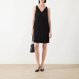 Model wearing black V-neck sleeveless mini dress, styled with black shoulder bag and black pointed-toe heels