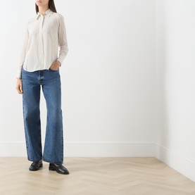 Model wearing Max Mara Studio Natural Stripe silk shirt with wide-leg blue jeans and black loafers.