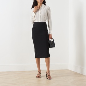 Model wearing Max Mara Studio black midi pencil skirt, styled with a striped shirt and strappy heels, carrying a small black handbag.