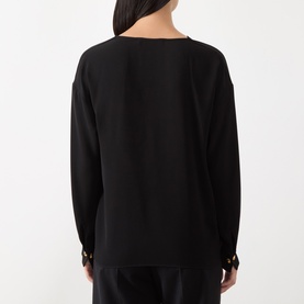 Model wearing Max Mara Studio black long-sleeve top, rear view, with gold button cuff detail, styled with black trousers.