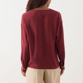 Model wearing Max Mara Studio ruby long-sleeve top, back view, with gold button cuff detail, styled with beige trousers.