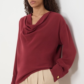 Model wearing Max Mara Studio ruby cowl-neck top with long sleeves and gold button cuff detail, styled with cream trousers.