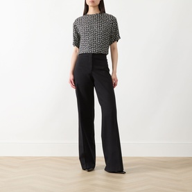 Model wearing Max Mara Studio Mambo Printed Blouse in black and white geometric print with short sleeves, styled with black wide-leg trousers.