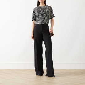 Model wearing Max Mara Studio Mambo Printed Blouse in black and white geometric print with black wide-leg trousers, holding a clutch bag.