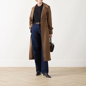 Model wearing camel longline trench coat, styled with dark shirt, wide-leg navy jeans and black heels, carrying dark brown bag