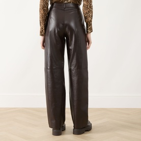 Model wearing Max Mara Studio brown faux leather wide-leg trousers, rear view, styled with a leopard print top and black chunky loafers.