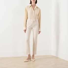 Model wearing Max Mara Studio Natural trousers in slim cropped cut, styled with a cream shirt and ivory heeled mules.