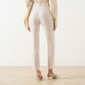 Model wearing Max Mara Studio natural tailored trousers, rear view, styled with a cream blouse and strappy heeled mules.