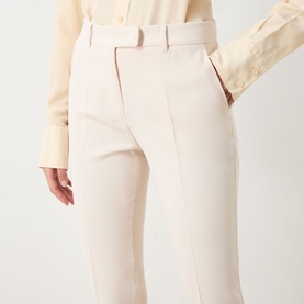 Model wearing Max Mara Studio natural trousers with tailored straight leg and belt loops, styled with a pale yellow shirt.