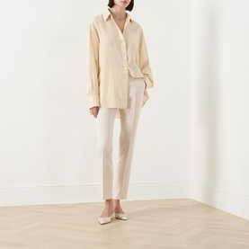 Model wearing Max Mara Studio Natural trousers in slim-cut silhouette, styled with an oversized cream shirt and ivory ballet flats.