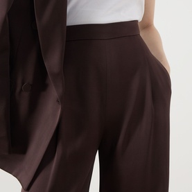 Model wearing Max Mara Studio chocolate wide-leg tailored trousers with pleat detail, styled with matching chocolate blazer and white top.