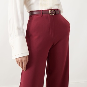 Model wearing Max Mara Studio Ruby wide-leg trousers, styled with a white blouse and dark leather belt with gold buckle.
