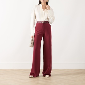 Model wearing Max Mara Studio Ruby wide-leg trousers, styled with a white shirt, brown belt and white flat shoes.
