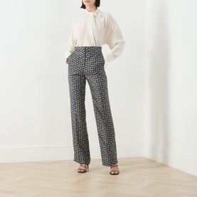 Model wearing Max Mara Studio black and white geometric print silk wide-leg trousers, styled with a cream blouse and strappy heels.