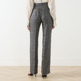 Model wearing Max Mara Studio black and white geometric print silk wide-leg trousers, rear view, styled with cream blouse and black heeled sandals.