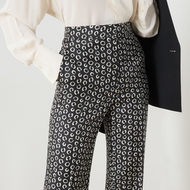 Model wearing Max Mara Studio black and white silk trousers with allover ring print, styled with white blouse and black blazer.