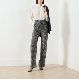 Model wearing Max Mara Studio black and white silk printed trousers, styled with a cream blouse, dark blazer and black heeled sandals.