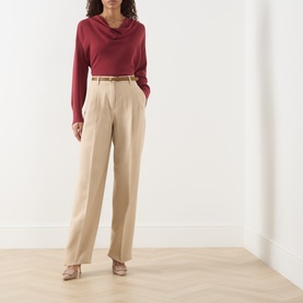 Model wearing Max Mara Studio Adunco Wide Leg Trousers in beige with pleated detail and belt, styled with a red cowl-neck top and nude heels.