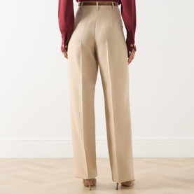 Model wearing Max Mara Studio Adunco Wide Leg Trousers in beige, back view, styled with a burgundy shirt and gold-tone belt.