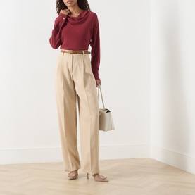 Model wearing Max Mara Studio Adunco Wide Leg Trousers in beige with pleats and belt, styled with a red cowl-neck top and grey bag.
