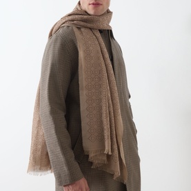 Model with Salvatore Ferragamo Geometric Logo Print Stole in beige, featuring tonal jacquard pattern and frayed edges, styled over olive knitwear