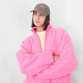 Model with Ganni Logo Washed Baseball Cap in Kalamata, styled with an oversized pink fleece zip-up jacket