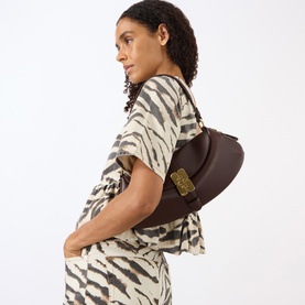 Model carrying Ganni B-Kat Logo Shoulder Bag in Chicory Coffee, gold-tone butterfly hardware, worn over shoulder, styled with zebra-print dress