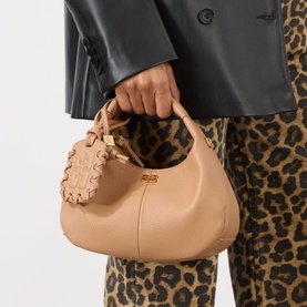 Model carrying Ganni Hobo Mini Crossbody Bag in Tawny Birch, gold-tone Butterfly hardware, top handle, styled with leopard print trousers.