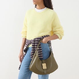 Model carrying Ganni Kat Small Hobo Bag in Military Olive with gold-tone butterfly clasp, styled with yellow jumper and jeans.