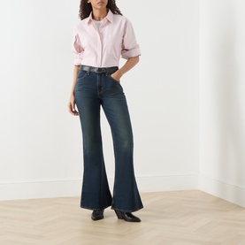 Model wearing Levis High Vibration flare jeans in dark indigo denim, styled with a pink shirt and black loafers