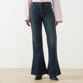 Model wearing Levi's High Vibration flare jeans in dark indigo denim, styled with a blush pink top and black shoes.
