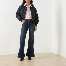 Model wearing Levi's High Vibration flare jeans in dark indigo denim, styled with a black bomber jacket, pink shirt, and black heels.
