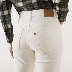 Model wearing Levi's cream flare jeans, rear view showing red tab logo patch, styled with a green plaid shirt.