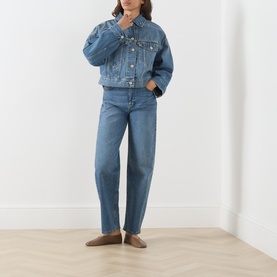 Model wearing Levi's Trip On Drip Trucker denim jacket in mid-blue wash, styled with matching blue jeans and taupe loafers.
