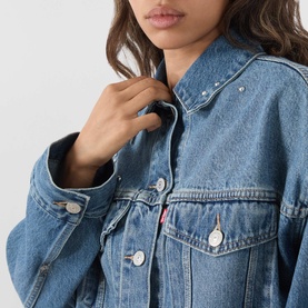 Model wearing Levi's Trip On Drip Trucker denim jacket in mid-blue wash, silver button detail, close-up chest and collar view.