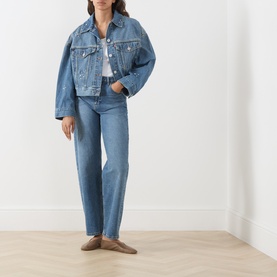 Model wearing Levi's Trip On Drip Trucker denim jacket in mid-blue wash, styled with matching straight-leg jeans and tan loafers.