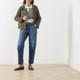 Model wearing Levi's jeans in Let's Fly mid-blue denim, styled with olive jacket, stripe top and black mules.