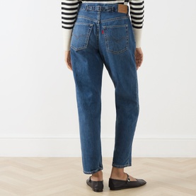 Model wearing Levi's jeans in Let's Fly mid blue denim, rear view, styled with a striped top and black loafers.