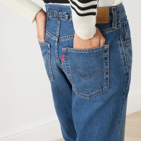 Model wearing Levi's jeans in Let's Fly mid-blue denim, showing back pocket detail with logo tab, styled with a striped knit top