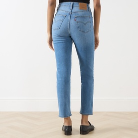 Model wearing Levi's slim-fit jeans in True Blue Mid denim, shown from behind with black loafers visible at hem