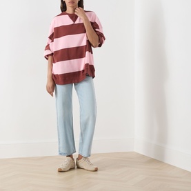 Model wearing Levi's straight leg jeans in light blue denim, styled with a pink and burgundy striped oversized tee and cream trainers.