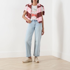 Model wearing Levi's straight jeans in light blue denim, styled with a pink striped shirt and graphic tee, with cream trainers.