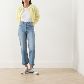 Model wearing a yellow knit cardigan with white T-shirt, light blue straight-leg jeans, and green striped trainers