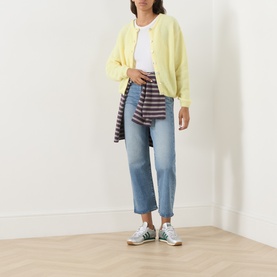 Model wearing a pale yellow oversized cardigan with blue cropped jeans, striped shirt tied at waist, and green trainers