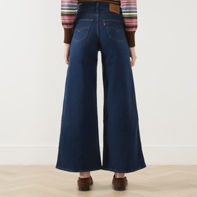 Model wearing Levi's True Blue Dark wide leg jeans, rear view, styled with a striped knit top and brown loafers