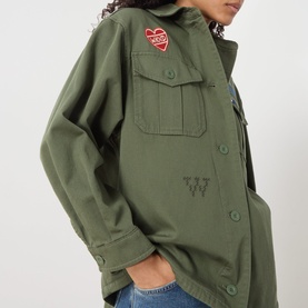 Model wearing Max Mara Weekend khaki cotton military jacket with heart patch, embroidered logo, and chest pockets, styled with blue jeans.