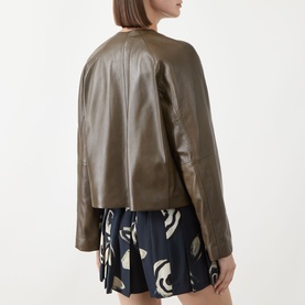 Model wearing Max Mara Main Bouquet Cropped Leather Jacket in kaki, collarless with smooth finish, styled with a printed mini skirt.